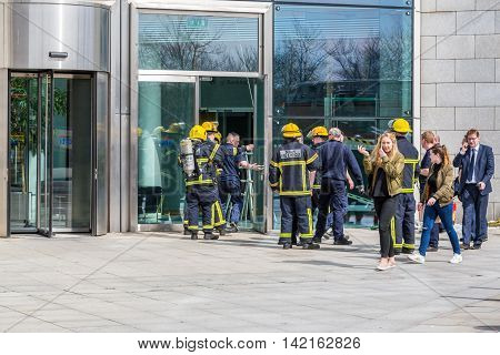 A group of firefighters outside a building.
Dublin, Ireland - April 21, 2016: Group of firefighters from Dublin Fire Brigade gathered outside a building. 
Firefighters talking. People passing by.