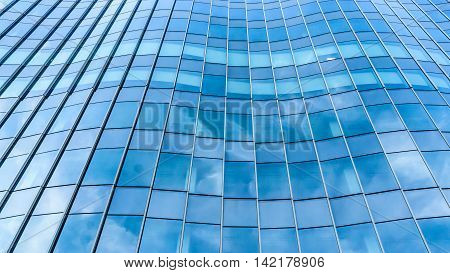 Perspective and underside angle view to textured background of contemporary glass facade of achitecture building skyscrapers with the light reflect of sky and cloud. (Detail curve shape of glass with vertical and horizontal mullion)