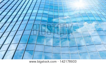 Perspective and underside angle view to textured background of contemporary glass facade of achitecture building skyscrapers with the light reflect of sky and cloud. (Detail curve shape of glass with vertical and horizontal mullion)
