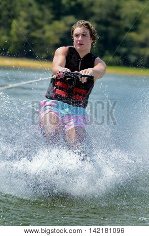 Teenage boy water skiing on a trick ski in a lake.