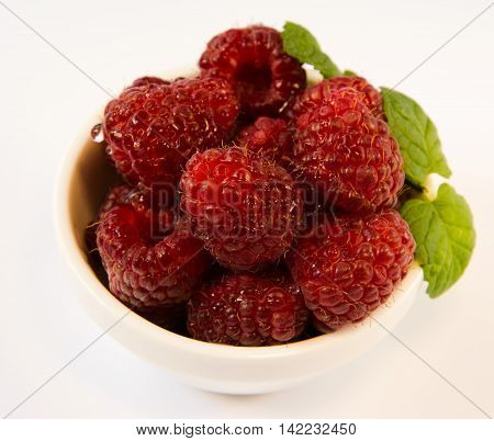 raspberries in a white plate with mint on a white table