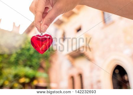 Holding a decoration in form of heart with Romeo and Juliet balcony on the background in Verona city