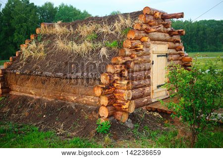 hut with dirt roof is collected from logs in forest on field