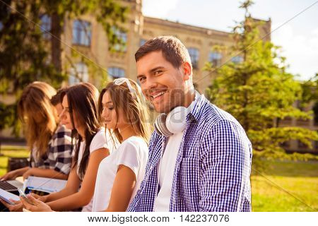 Happy Student Sitting On Bench Near College And Prepare For Tests Together With Friends