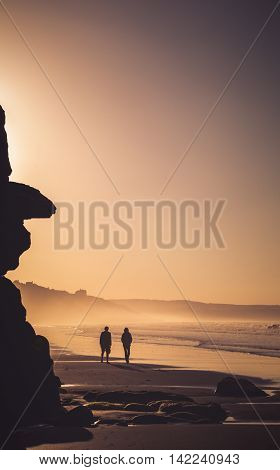 A couple in silhouette wandering along the beach