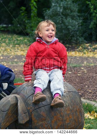 Little girl siting on wooden statue of sheep in outdoor playgraud