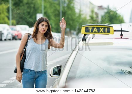 Young Woman Raising Arm To Hail Taxi On Street