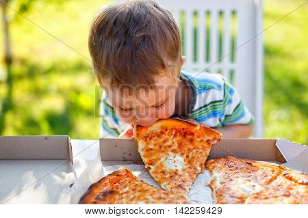kid biting a slice of pizza. funny toddler eats pizza without using his hands