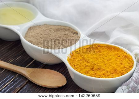 Turmeric black pepper and olive oil in white ceramic bowl on wooden background. Ingredients for golden paste