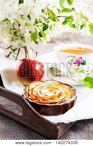 Apple rose shaped pie and cup of tea on the vintage serving tray. Breakfast tea with sweet apple pastry. Homemade apple cake for tea time.