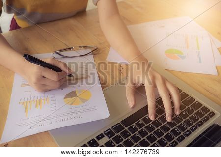 close up hand of business women and laptop computer and write on paper garph chart on wooden desk outdoor office with morning light. vintage filter effect.