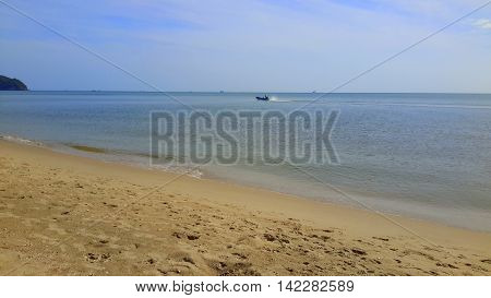 distant small fishing boat with standing man, speeding past on a flat sea, sandy beach in foreground, island barely seen on the left, Songkhla, Thailand