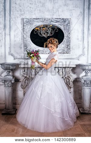 Bride standing next to the fireplace in a luxurious wedding dress. gray room