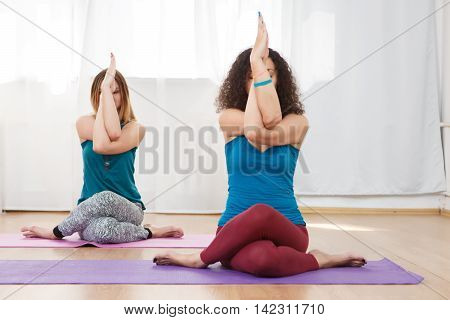 Two young caucasian women practicing eagle pose, garudasana, in yoga class