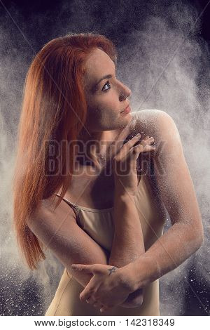 Portrait of a redheaded woman dancer. Girl dancer posing in beige bathing suit on a black background. Studio portrait of woman dancing with flour.