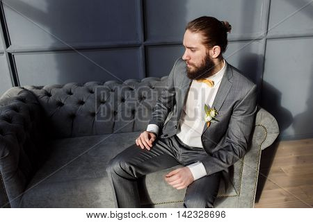 Handsome strong brutal bearded man sitting on the grey sofa in hotel room