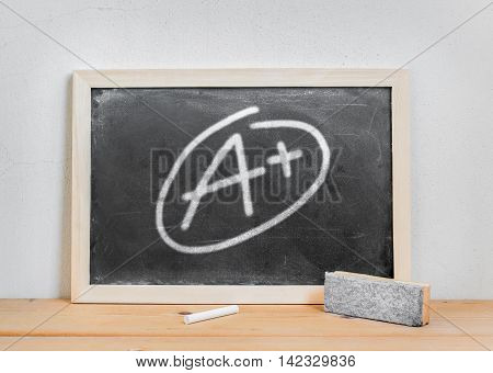 Grade a plus write on dirty blackboard chalk and eraser on wood table over white cement background