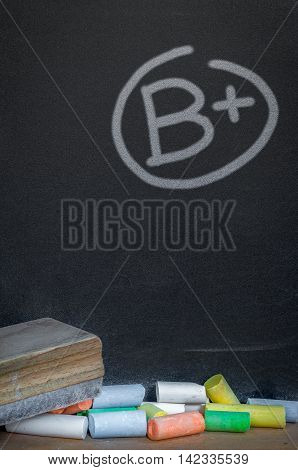 Colorful of chalk on wood table over grade b plus on black chalkboard background