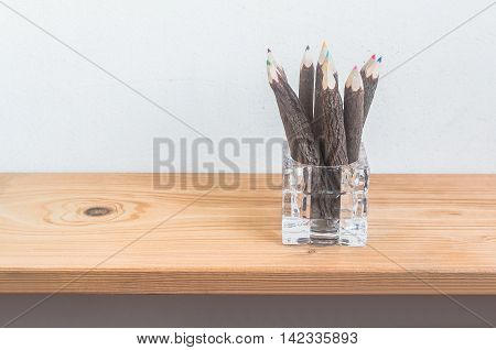 Color pencils in pencil holder from glass on wooden shelf over grunge cement wall