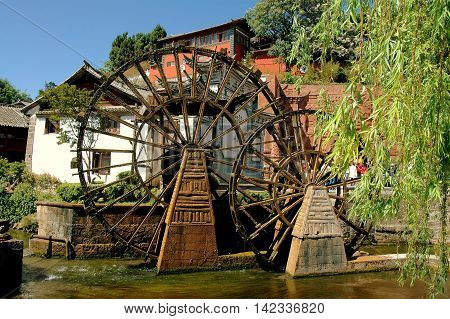 Lijiang China - April 19 2006: Two traditional Chinese wooden water wheels churn water in a stream flowing through Si Feng Square