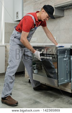 Installation of household appliances. Workman installing a built-in electric oven.