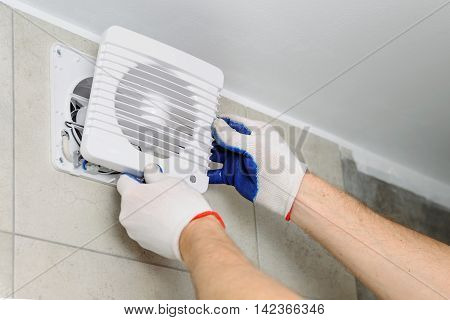 Installation of household appliances. Workman fixing the exhaust fan on the wall.
