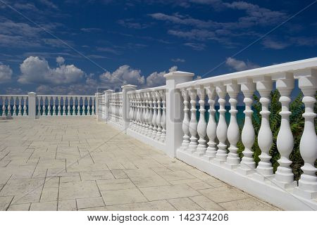 White decorative fence on the waterfront of the Anapa city resort on the Black Sea coast. Blue cloudy sky water with an emerald hue green tree leaves. Selective Focus on foreground.
