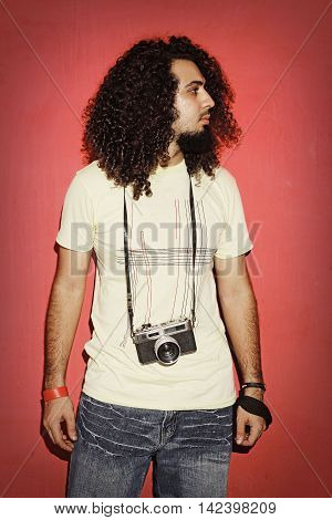 Closeup of one handsome passionate expressive cool young brunette photographer men with long curly hair holding a vintage SLR camera standing against red background