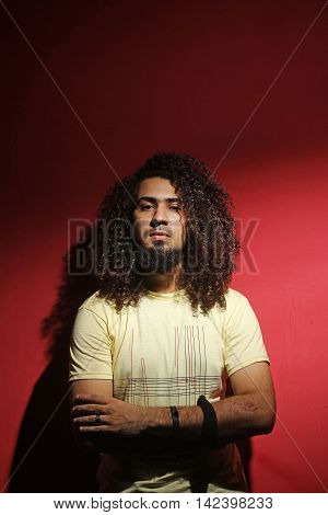 Sexy brunette young guy fashion and long beautiful curly hair against red background looking into the camera