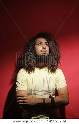 Sexy brunette young guy fashion and long beautiful curly hair against red background looking up