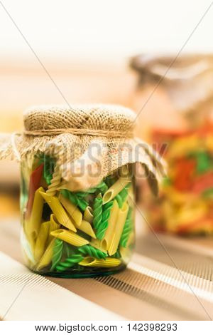 Dry colored pasta in a glass jar on the table
