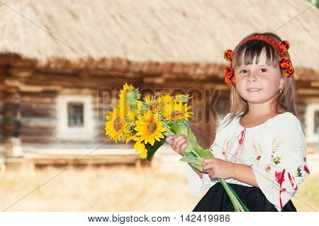 Girl with sunflowers and Hutsul wreath in the village with old wooden house