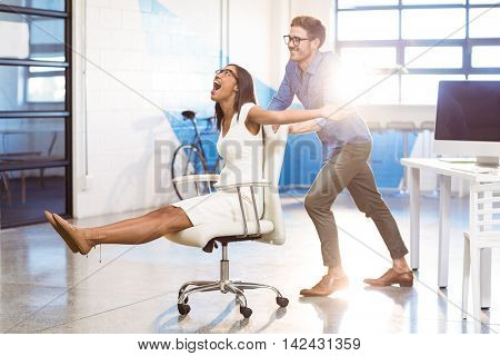 Business executive pushing businesswoman in office chair at workplace