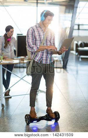 Smiling man standing on hoverboard and using laptop in office