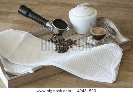 Glass of espresso, brown sugar, coffee beans, grouphead and sugar bowl on a wooden tray