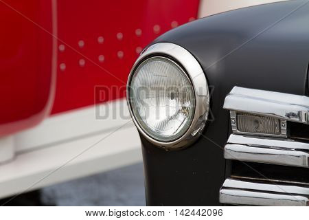 Section of an old car showing the vintage round headlight and matt black bonnet or hood.