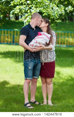Happy Couple Holding Their Newborn Daughter In Her Arms. Outdoors