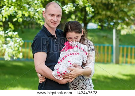 Happy Couple Holding Their Newborn Daughter In Her Arms. Outdoors