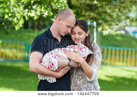 Happy Couple Holding Their Newborn Daughter In Her Arms. Outdoors