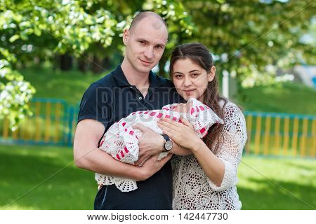 Happy Couple Holding Their Newborn Daughter In Her Arms. Outdoors