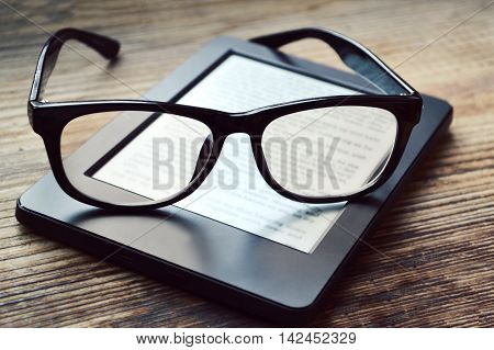Black ereader with retro glasses on wooden table