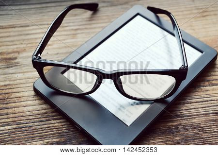 Black ereader with retro glasses on wooden table