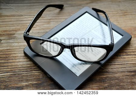 Black ereader with retro glasses on wooden table