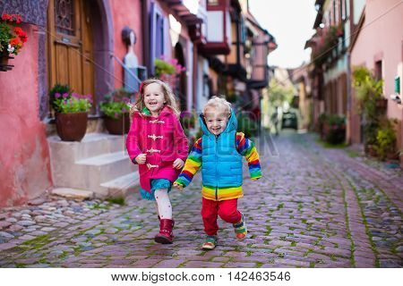 Cute little girl and boy walking down a street in historical medieval city center on cold autumn day. Children during fall vacation in Eguisheim Alsace France. Travelling and tourism with kids.