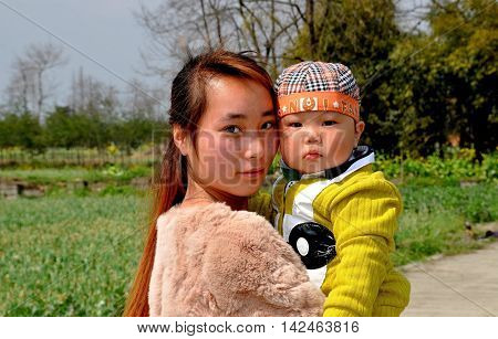Pengzhou China - March 14 2014: Young Chinese mother with freckled face holding her baby son at a Sichuan province farm