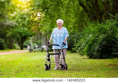 Happy senior handicapped lady with a walking disability enjoying a walk in a sunny park pushing her walker or wheel chair aid and support during retirement concept.