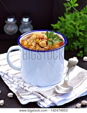 Soup with chickpeas, lentils, rice, beef in a bowl on a black background.