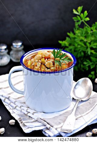 Soup with chickpeas, lentils, rice, beef in a bowl on a black background.