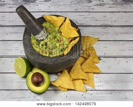 Guacamole with tortilla chips in authentic granite molcajete mortar on old wooden background