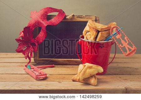 Hamantaschen cookies in bucket with grogge chalkboard and carnival mask